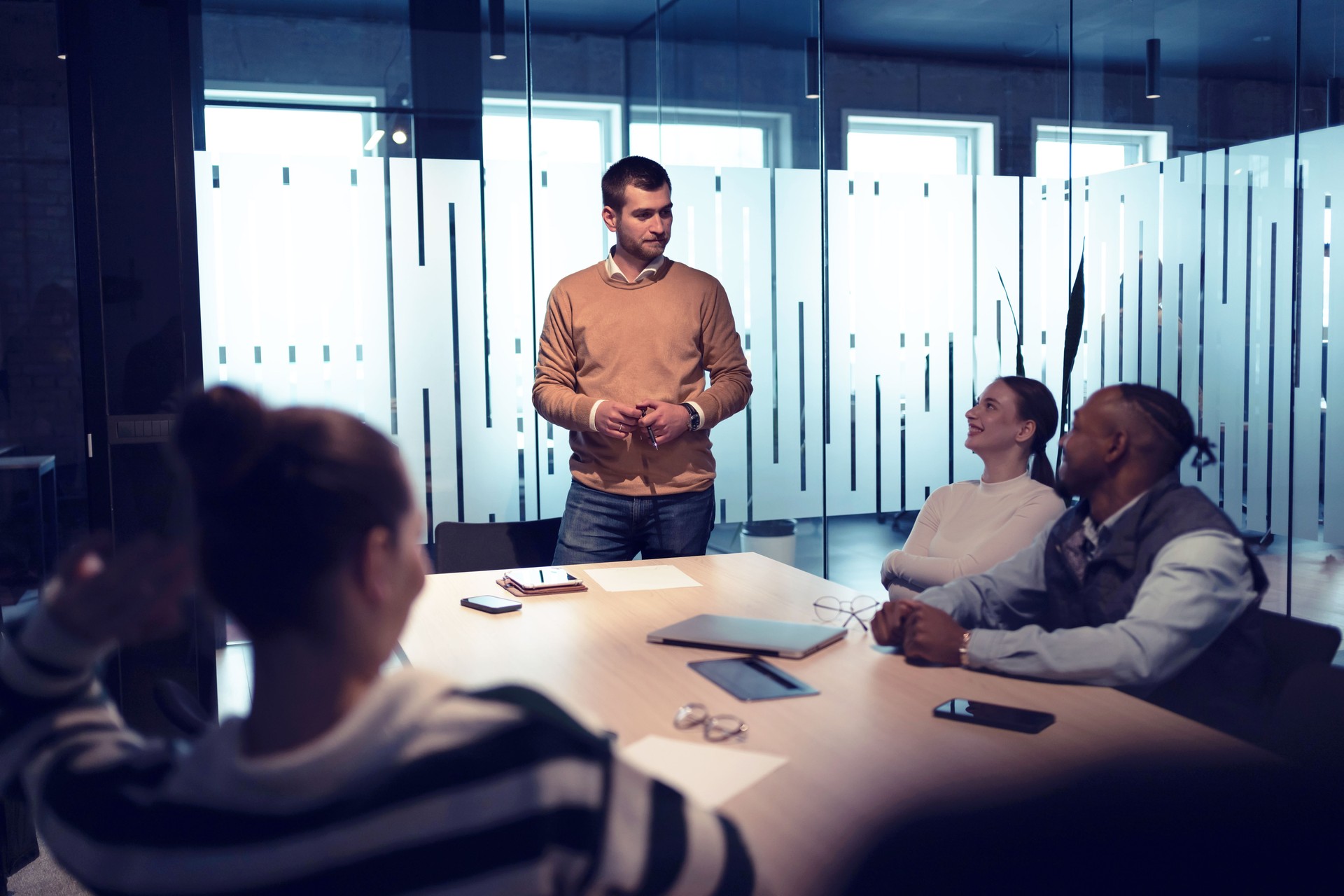 A diverse team of young professionals collaborates in a modern office conference room. Businesspeople discuss strategy, technology, and planning, using laptops to develop an innovative e-commerce project
